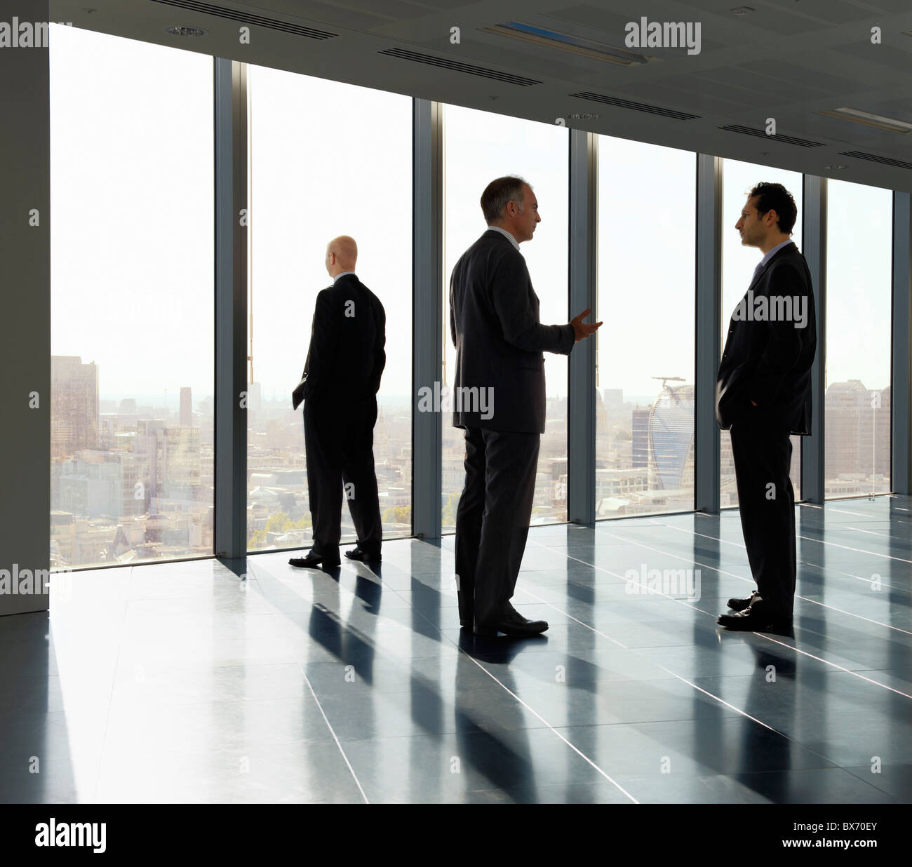 Three executives standing by window in empty office space with view over city landscape Stock Photo