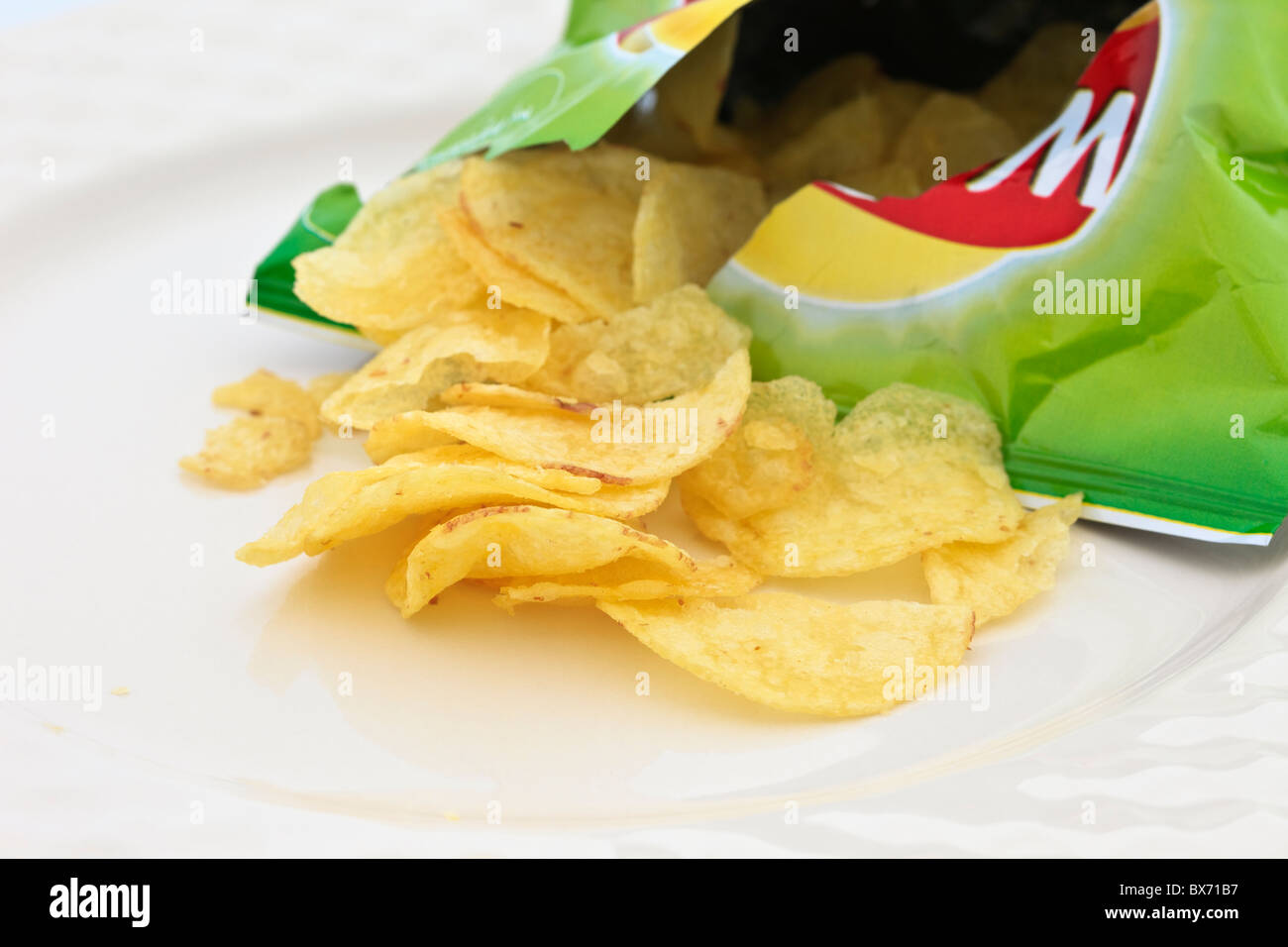 Walkers crisp packet open with potato crisps spilling out on a plate. England UK Stock Photo