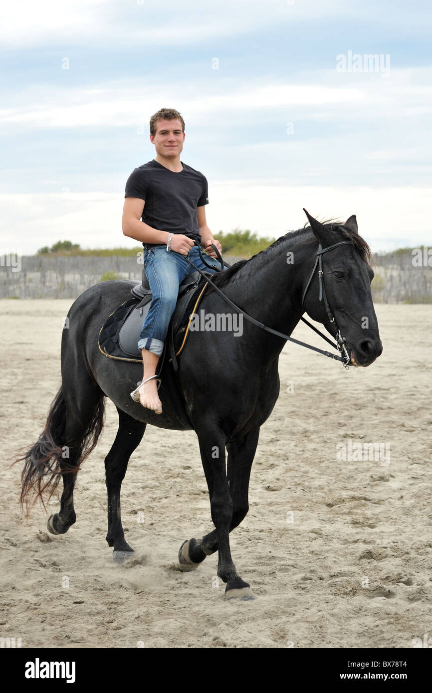 young man and his black stallion on the beach Stock Photo
