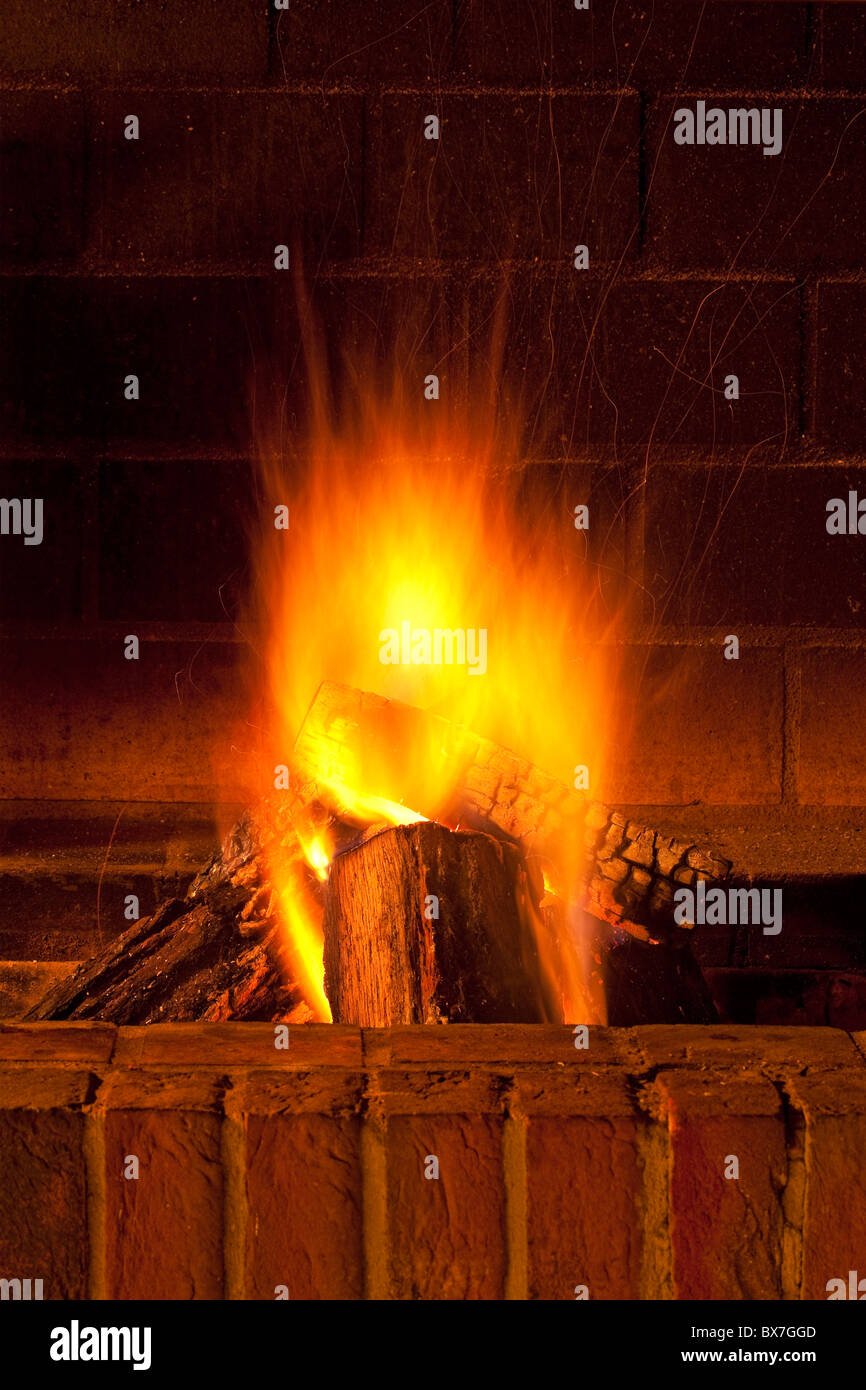 brick fireplace with large pieces of wood burning giving warmth Stock
