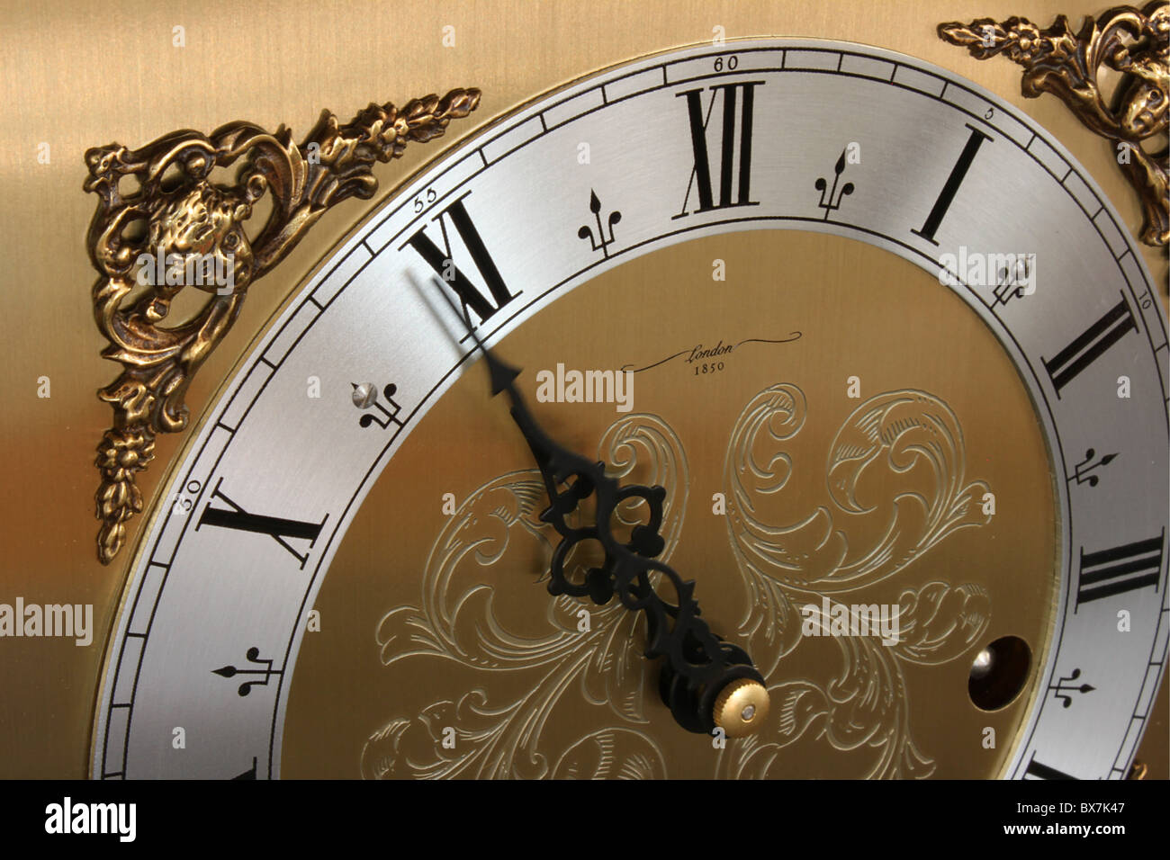 Partial view of an engraved brass clock face with Roman numerals and ornate hands reading 10:55 Stock Photo