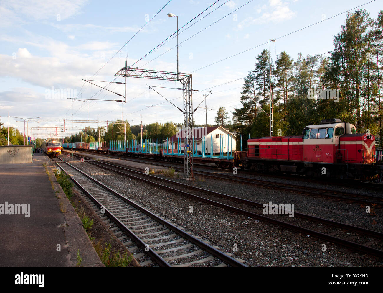 Railway station and cargo train waiting for the oncoming passenger train to pass it , Finland Stock Photo