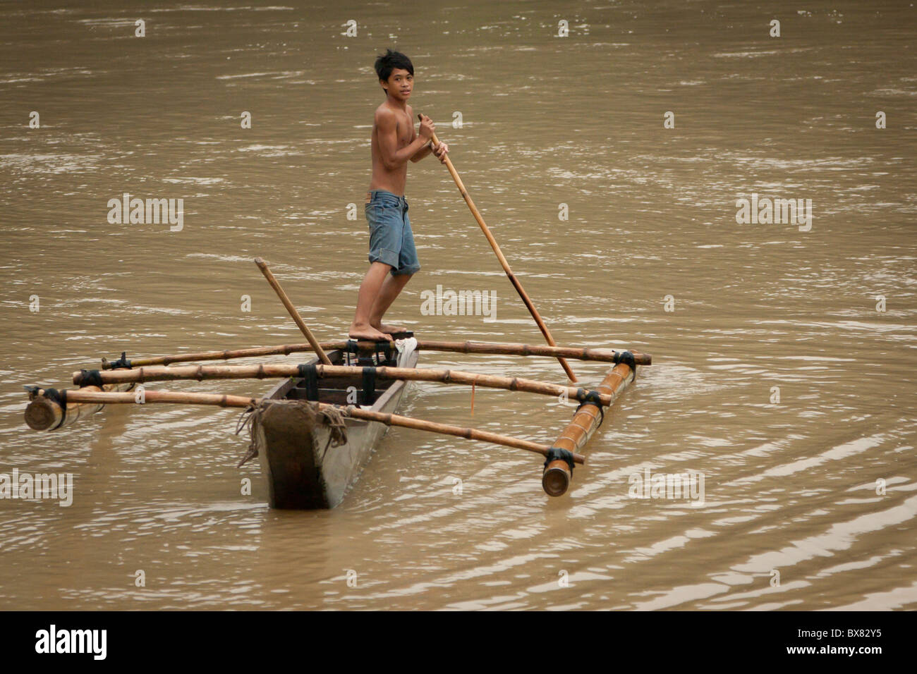 A boy maneuvers a small canoe in river with a bamboo pole Stock Photo -  Alamy