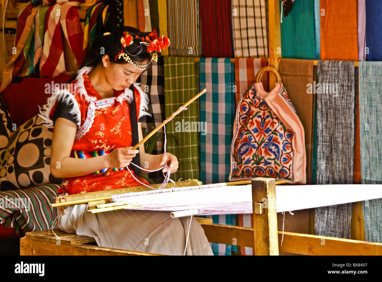 Young woman weaving in textile shop, Lijiang, Yunnan, China Stock Photo