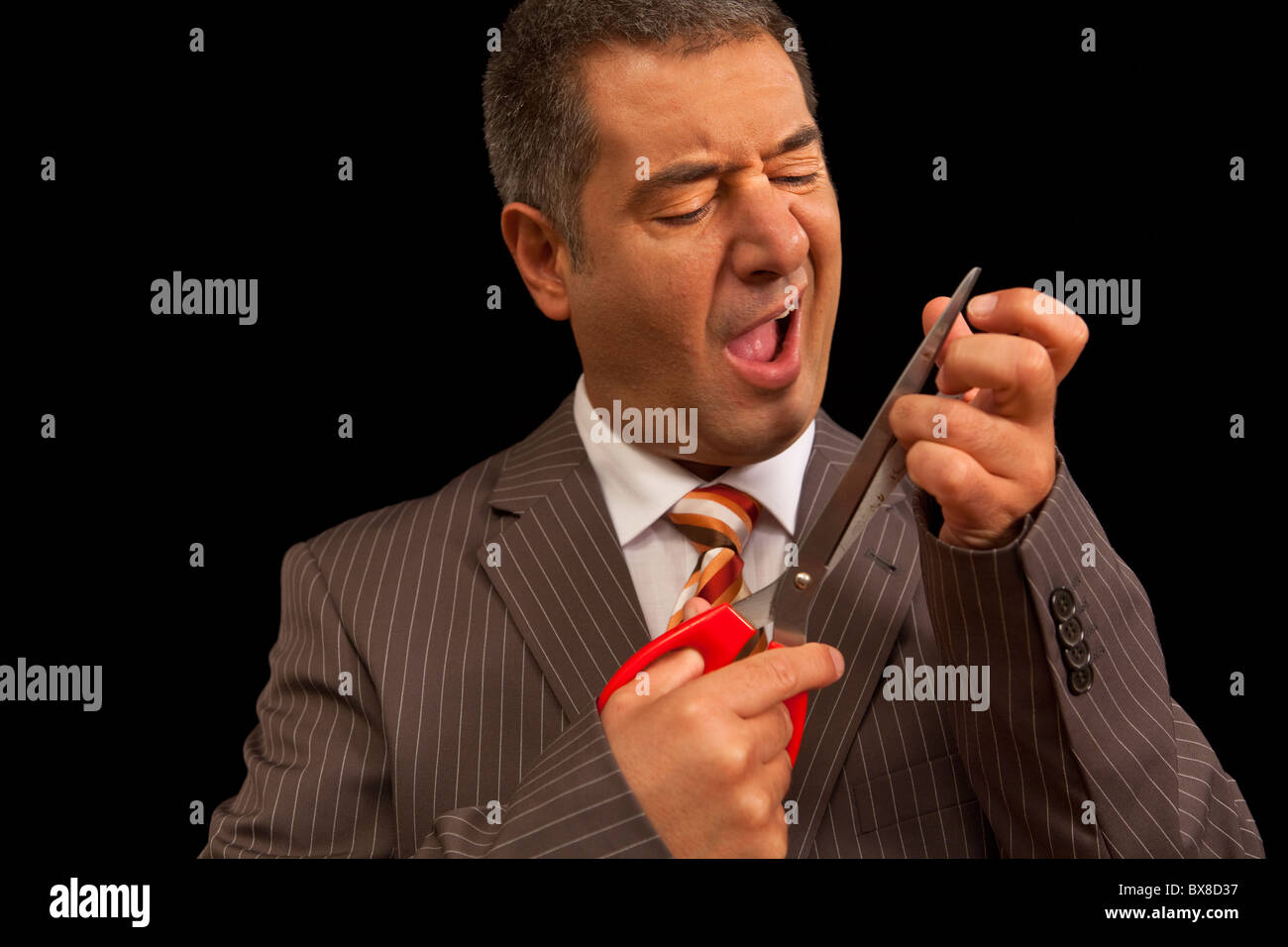 Businessman cutting nails with huge scisors, just hurt himself - Humour - Bodycare Stock Photo