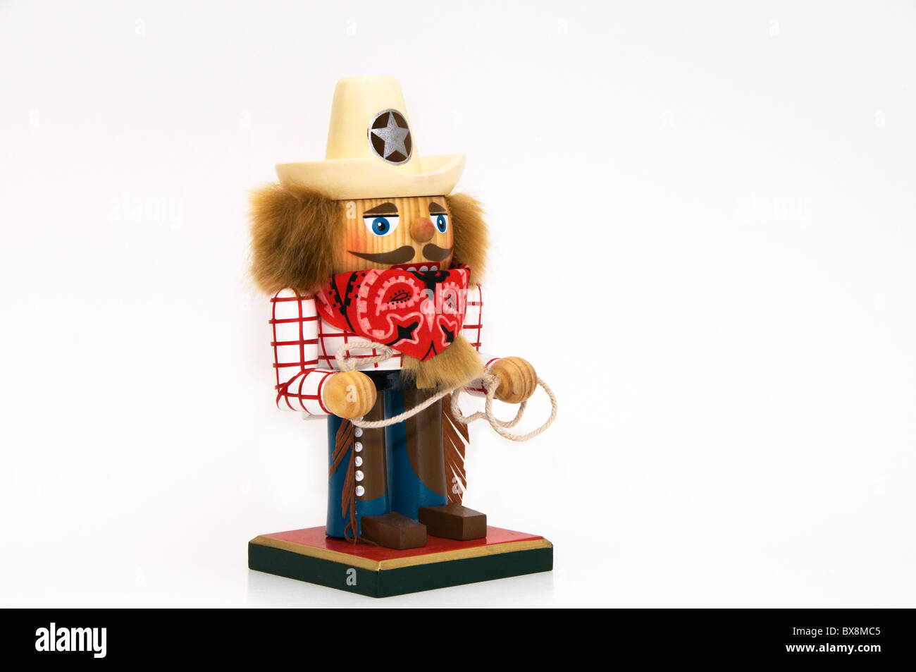 A charming holiday nutcracker dressed in western clothing and wearing a sheriff hat and red bandanna scarf holds a lasso rope. Stock Photo