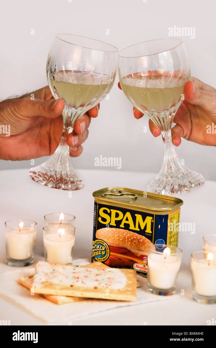 A couple toasts with wine glasses before a meal of Spam and Pop-Tarts by candlelight. Stock Photo