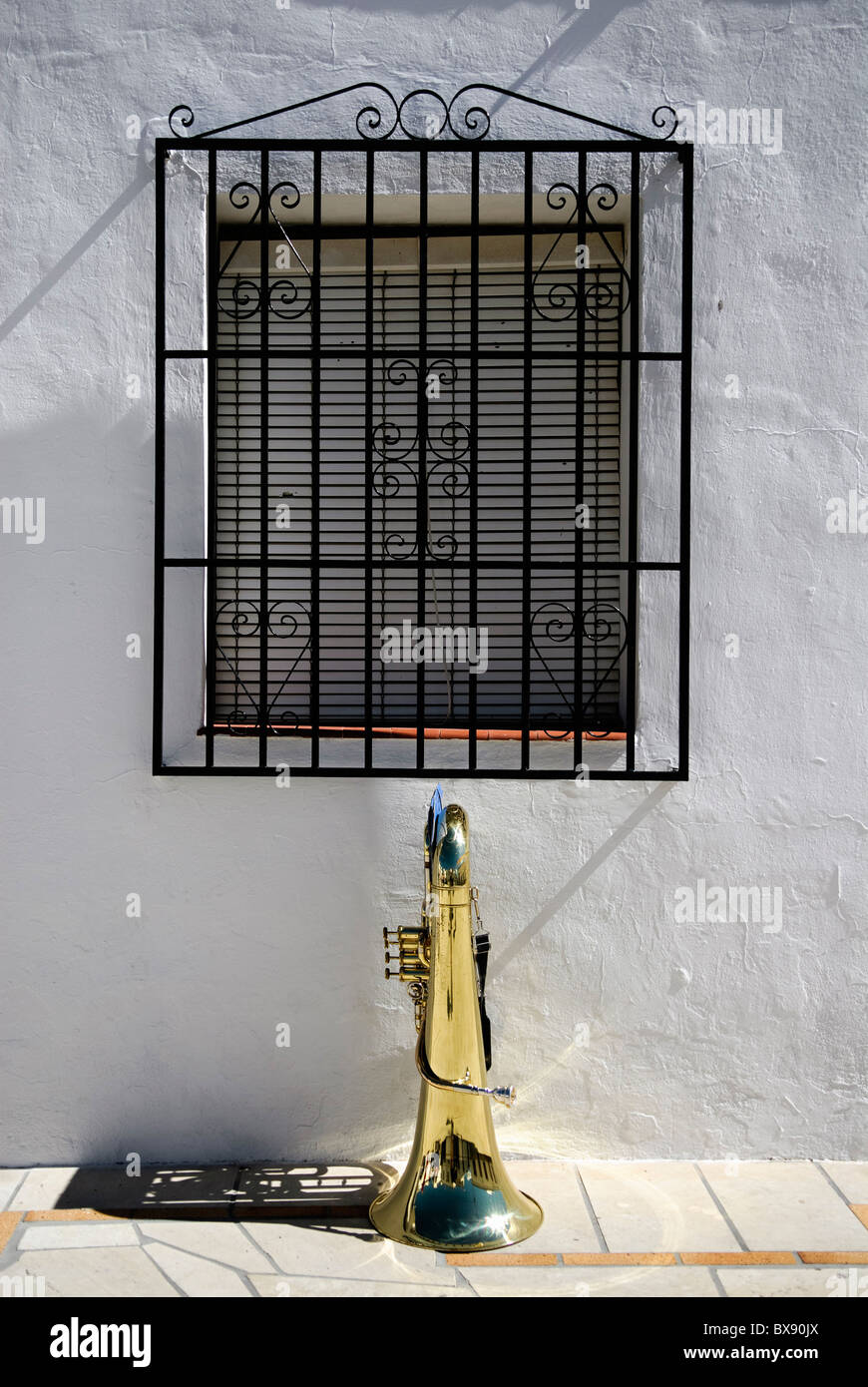 brass tuba stands in front of barred window in small spanish illage