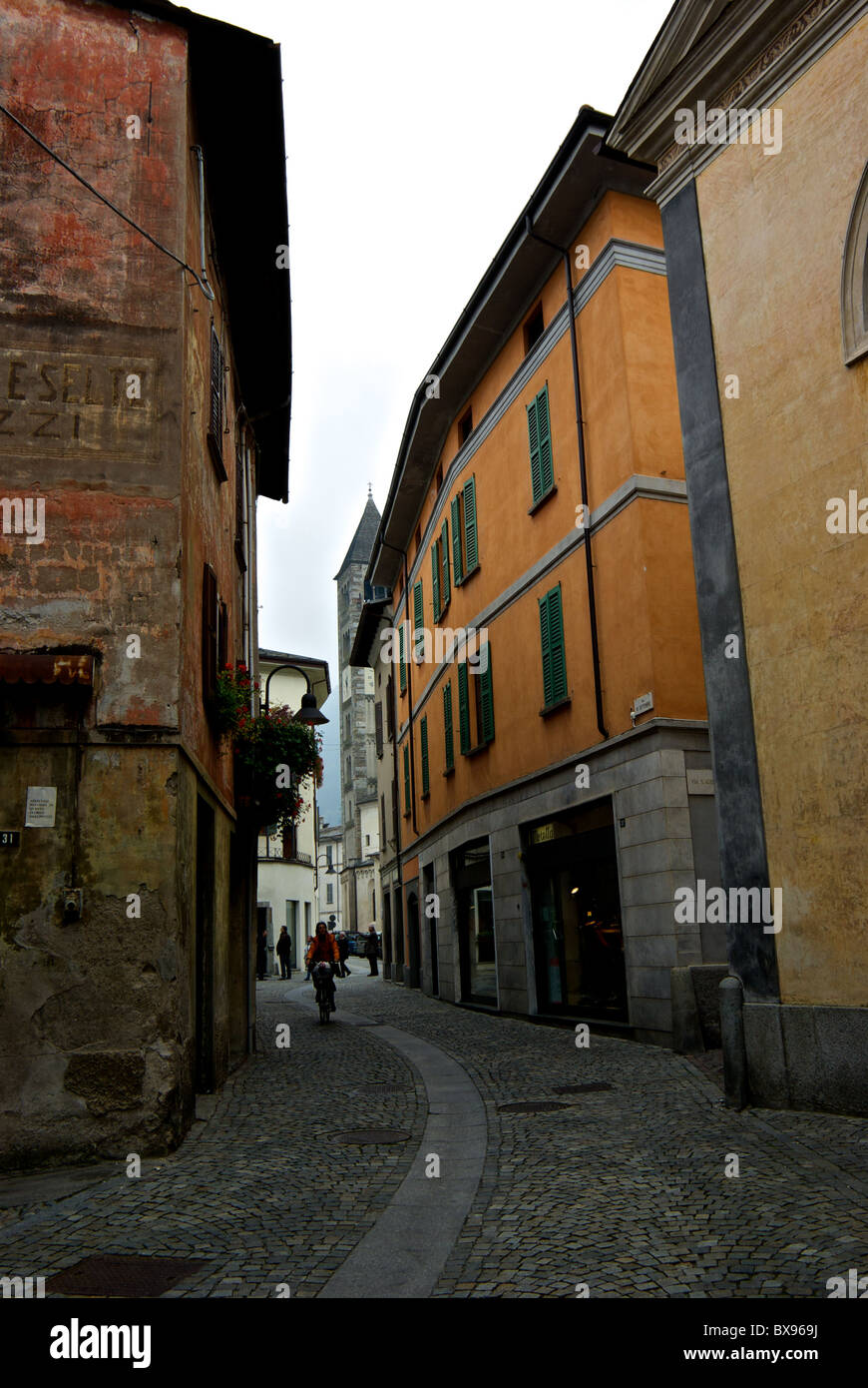 Narrow pedestrian cycling cobble stone passageway between old and renovated residential stucco apartments buildings Tirano Italy Stock Photo