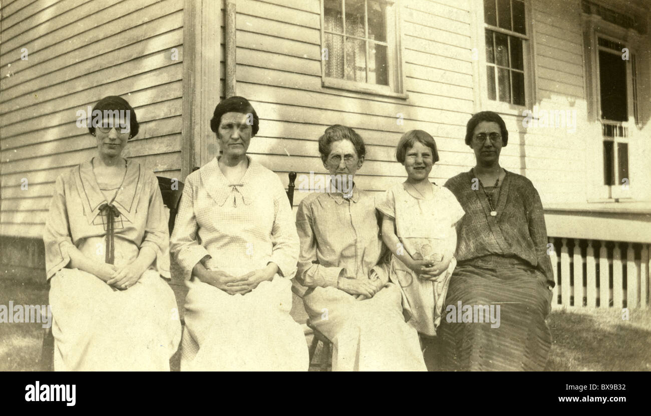 Three generations of women seated on chair outside wooden house during the 1920s 1930s homemade dresses family portrait American Stock Photo