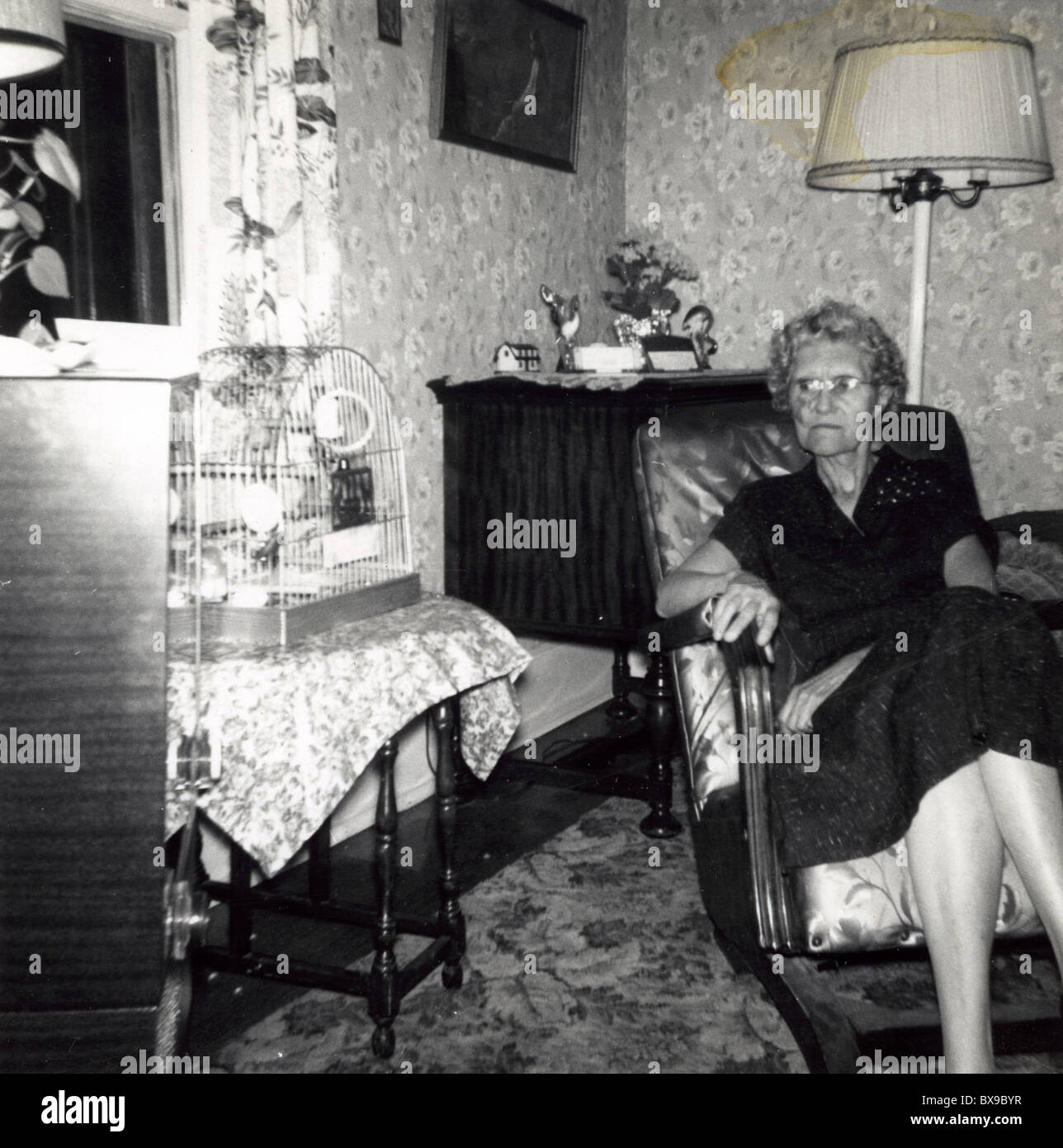 Old woman looking at empty bird cage. aging alone female house Americana black and white 1950s Stock Photo