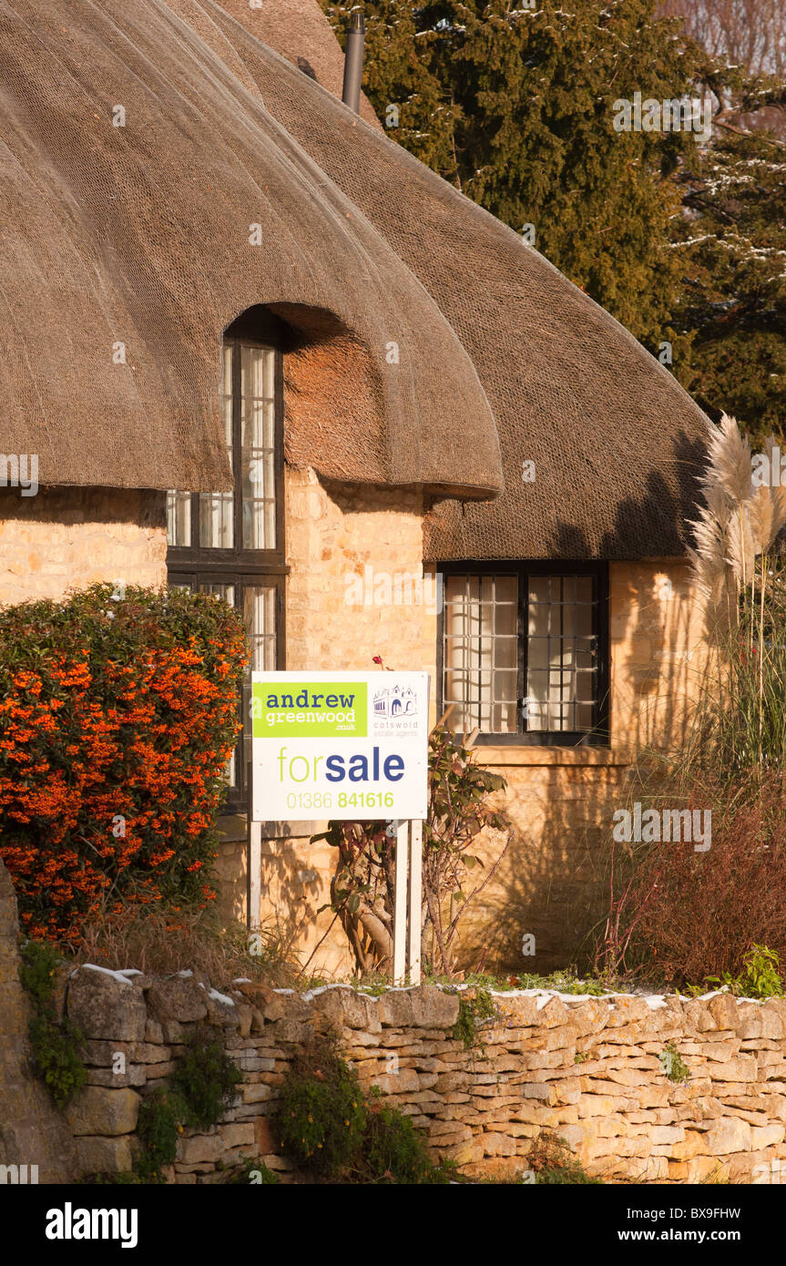 A 'For Sale' board on a thatched cottage in the Cotswold village of