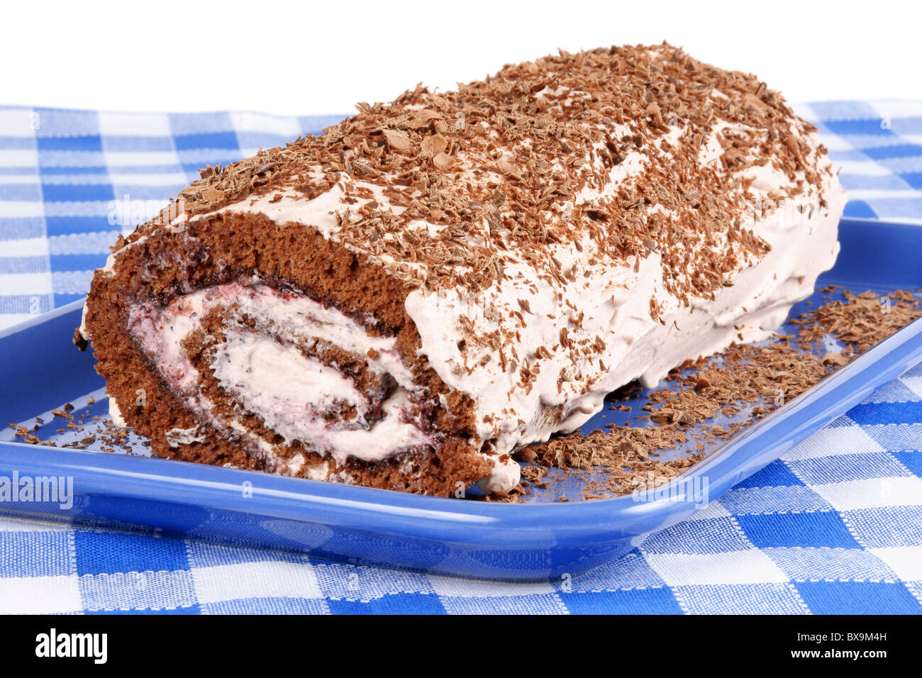 Chocolate swiss roll cake with berries marmalade and whipped cream served on a blue plate over a chequered background Stock Photo