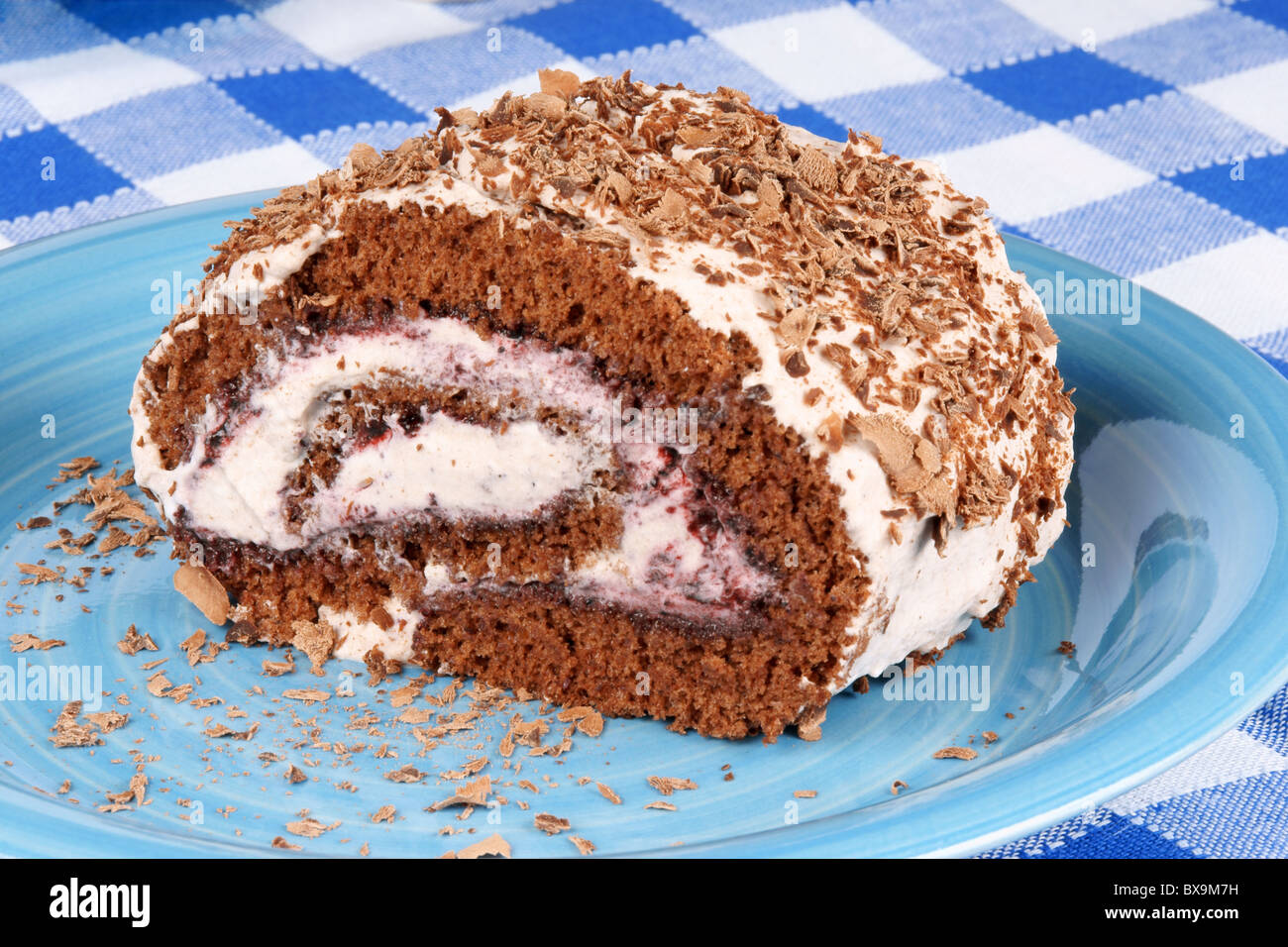 Chocolate swiss roll cake with berries marmalade and whipped cream over a chequered background Stock Photo