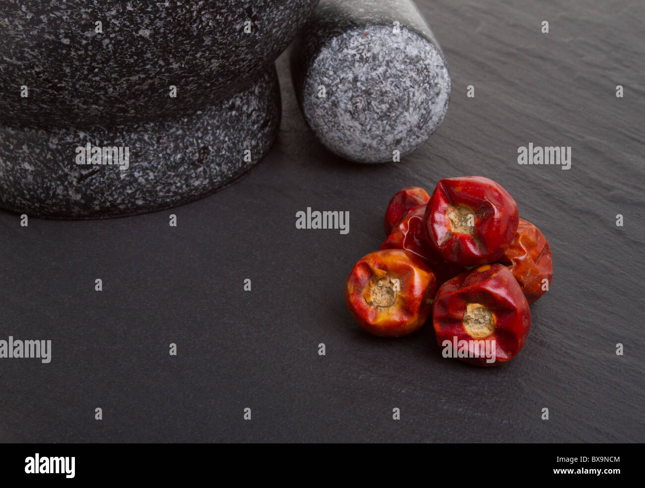 Dried vibrant Chilli's on dark slate background with mortar and pestle. Stock Photo