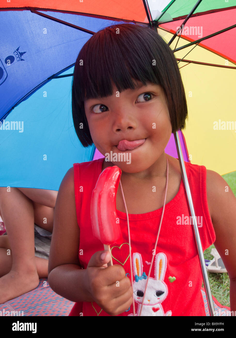 The girl licking her lollipop ice cream and holding her multi color umbrella Stock Photo