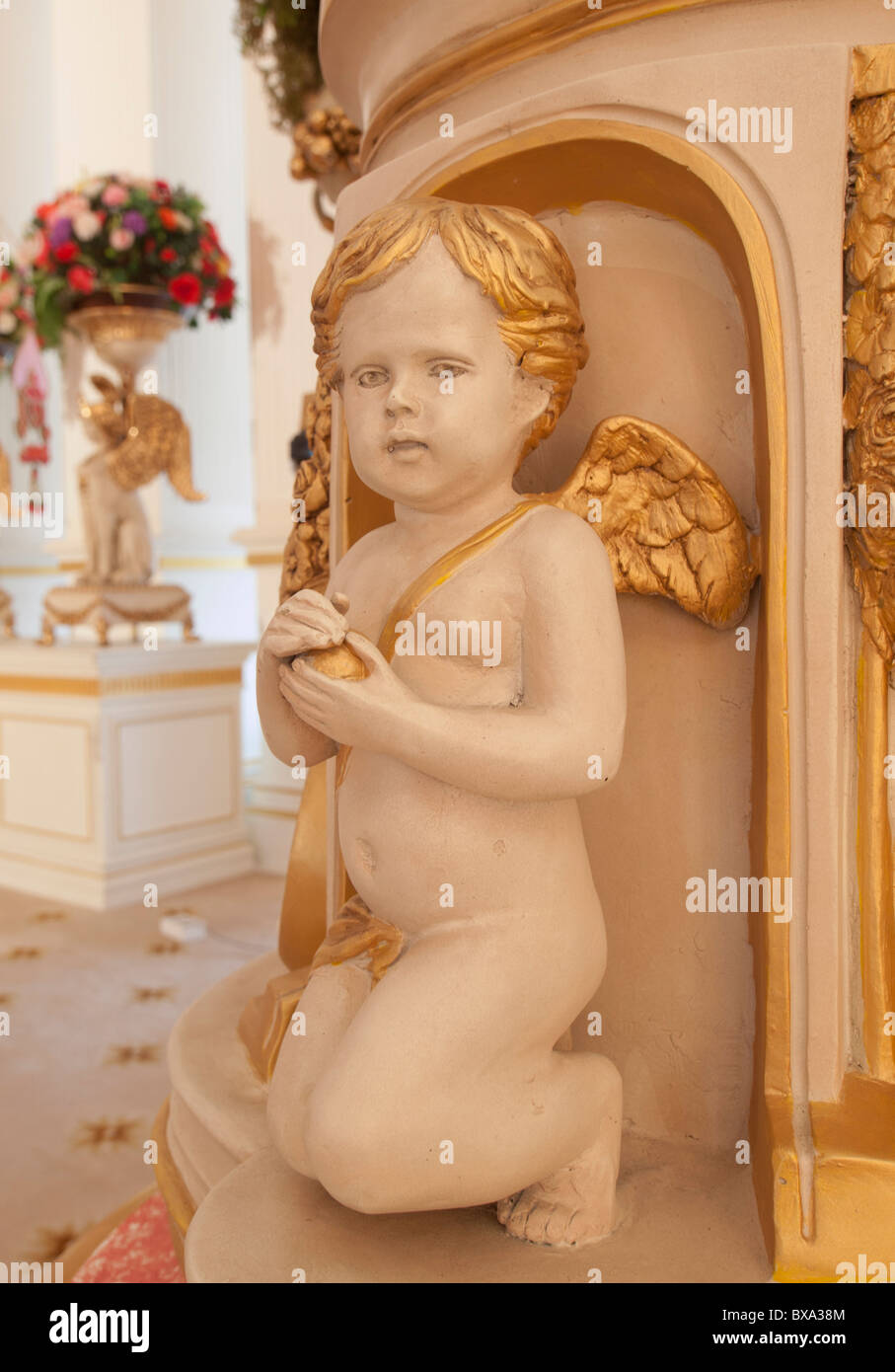 The childlike cherub indoor statue holding gold ball, looking cute in soft white color Stock Photo