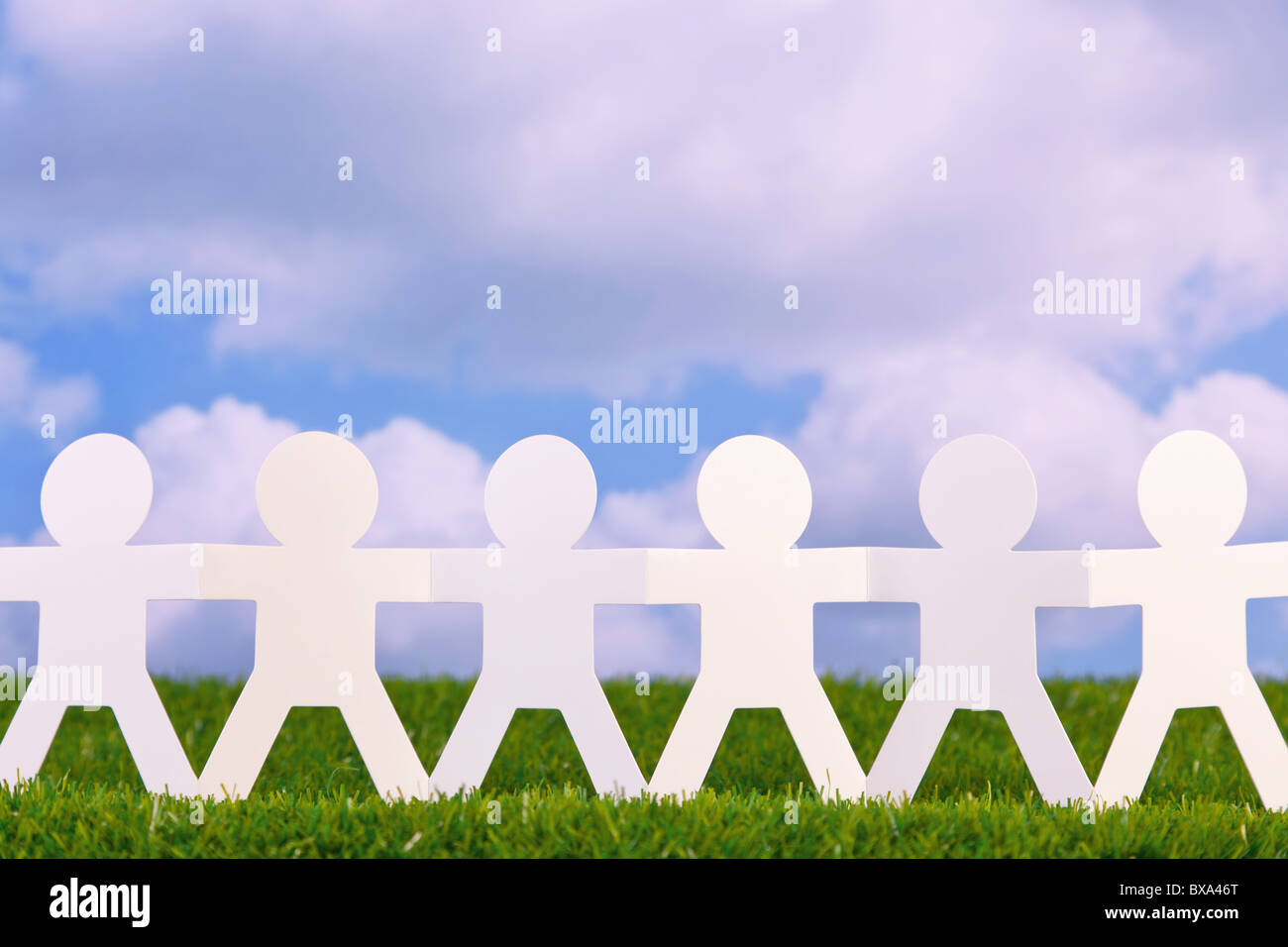 Concept image of paper men holding hands in a field with sky background Stock Photo