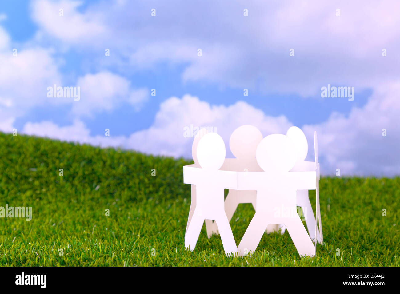 Concept image circle of paper men holding hands in a field with sky background Stock Photo