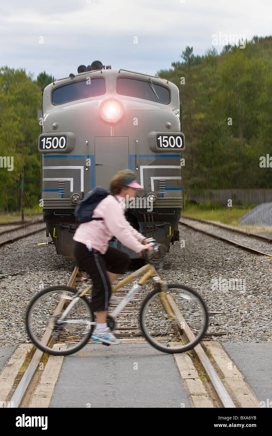 Woman riding bicycle across railroad tracks in front of train coming towards her Stock Photo