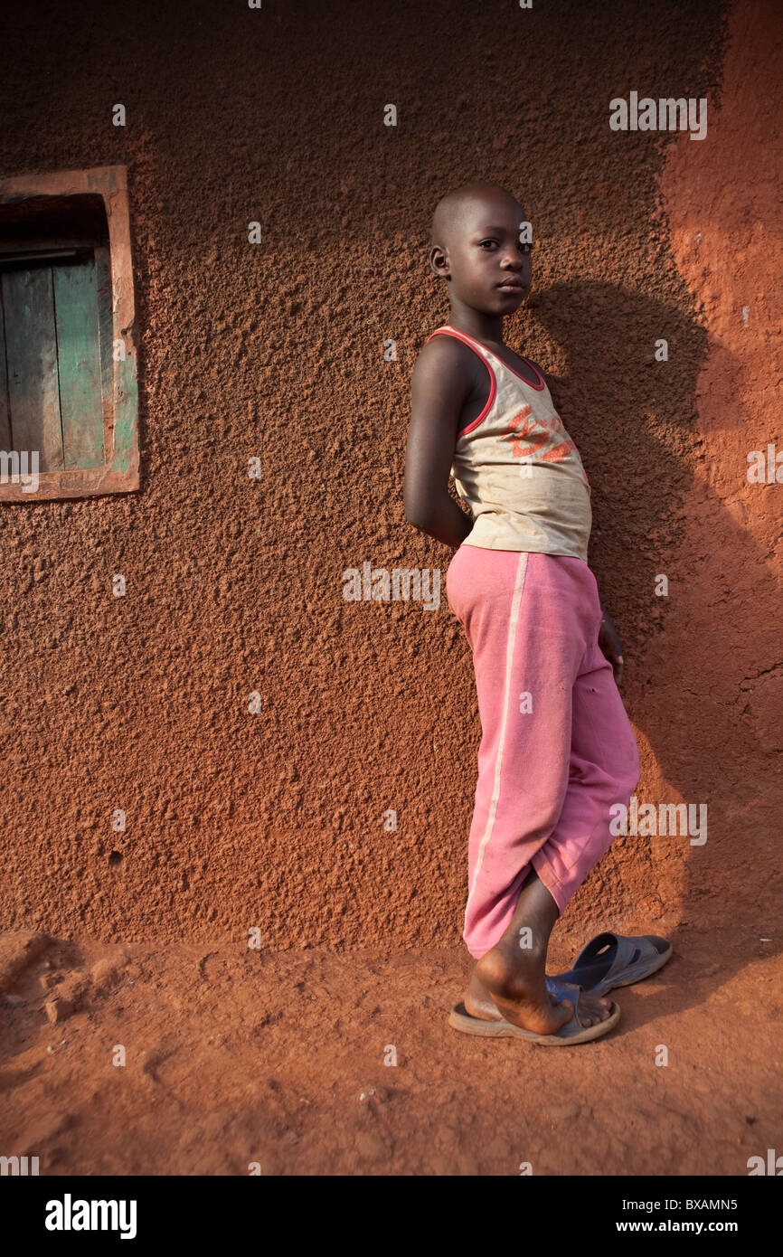 A boy stands alone outside a mud house in Jinja, Uganda, East Africa Stock Photo