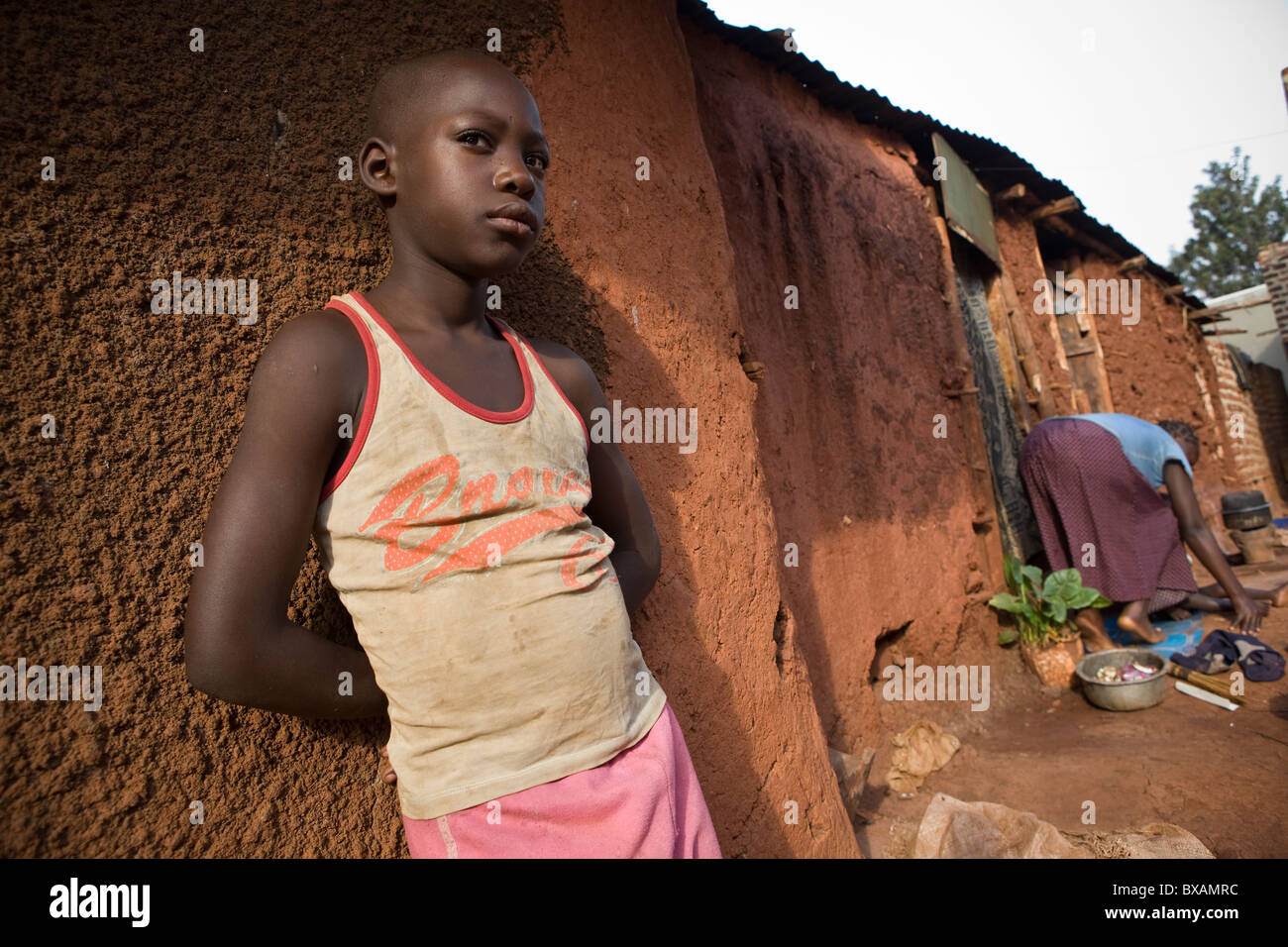 A boy stands alone outside a mud house in Jinja, Uganda, East Africa. Stock Photo