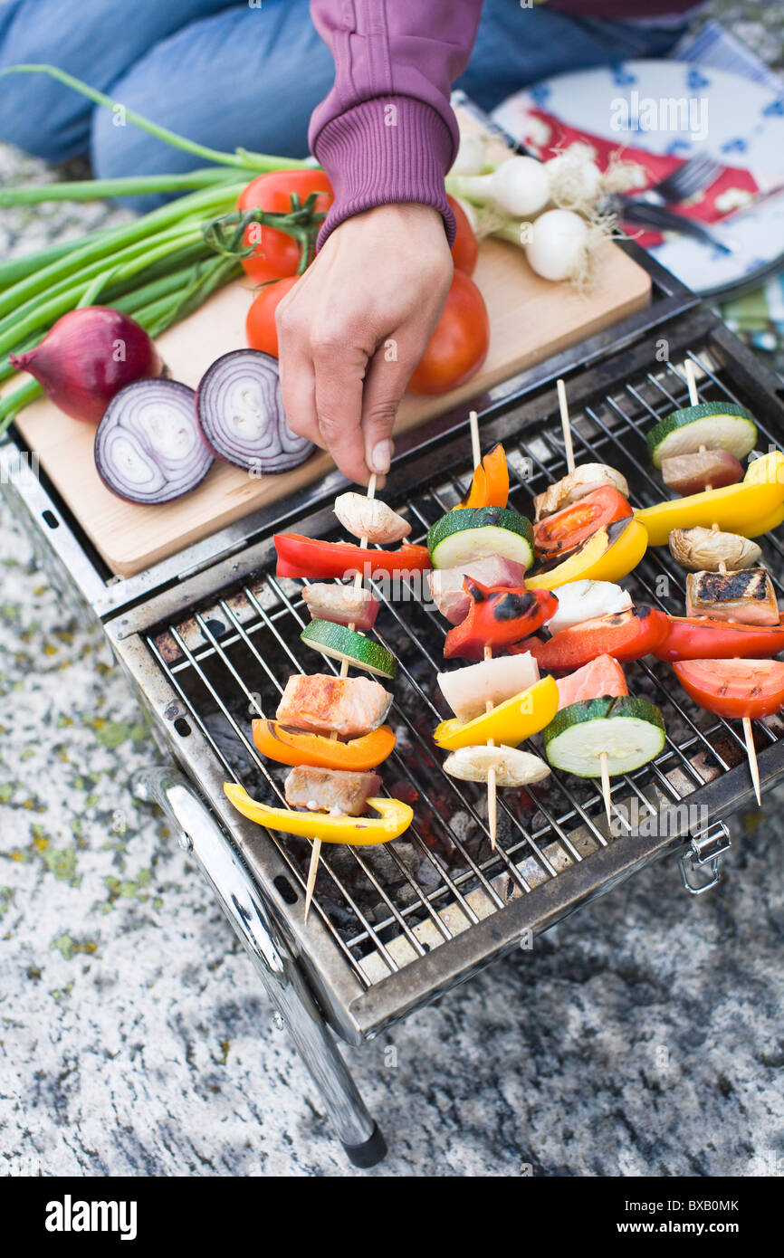 Person holding skewer with vegetables on grill Stock Photo