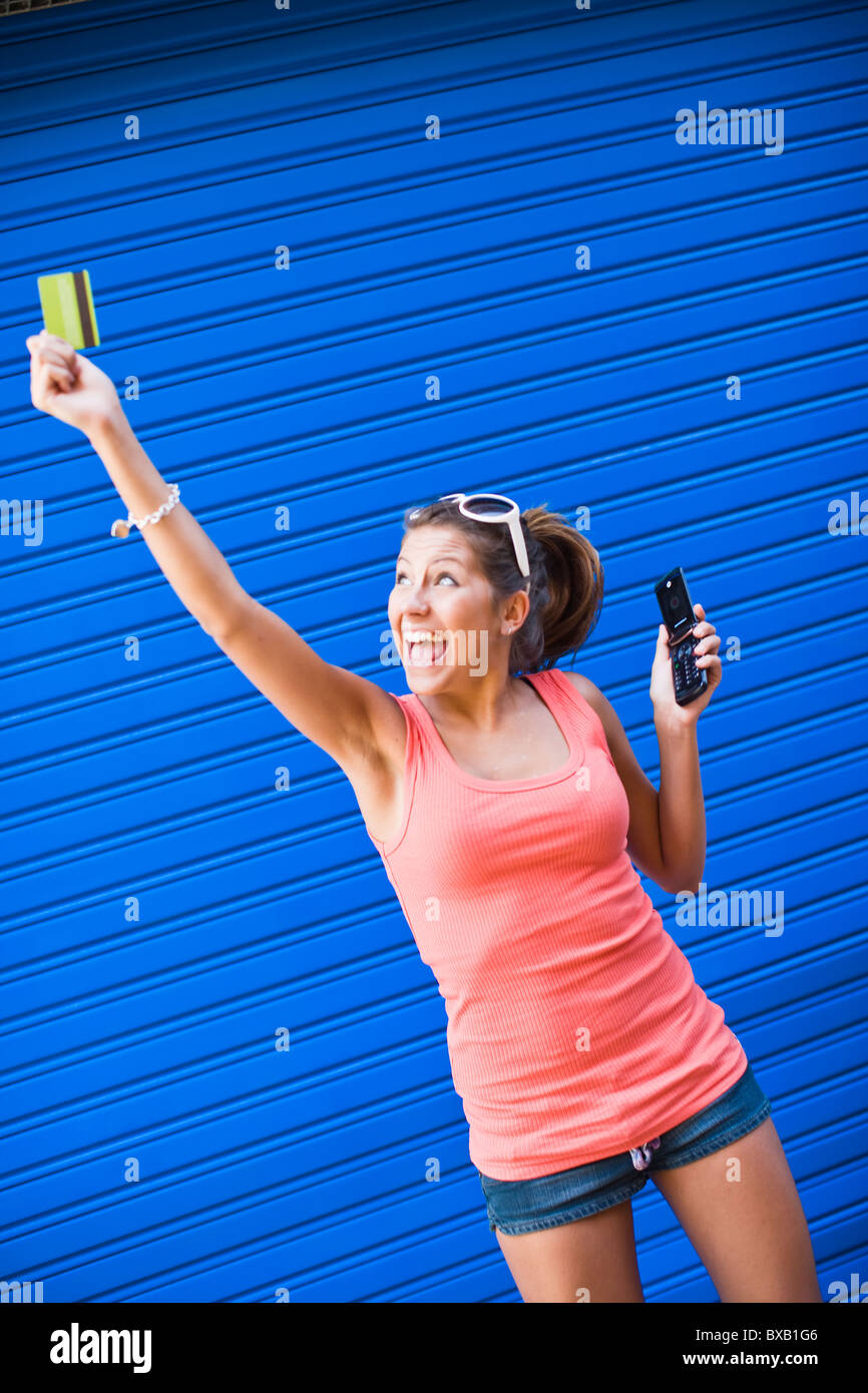 Young woman in front of blue wall, holding credit card and cell phone Stock Photo