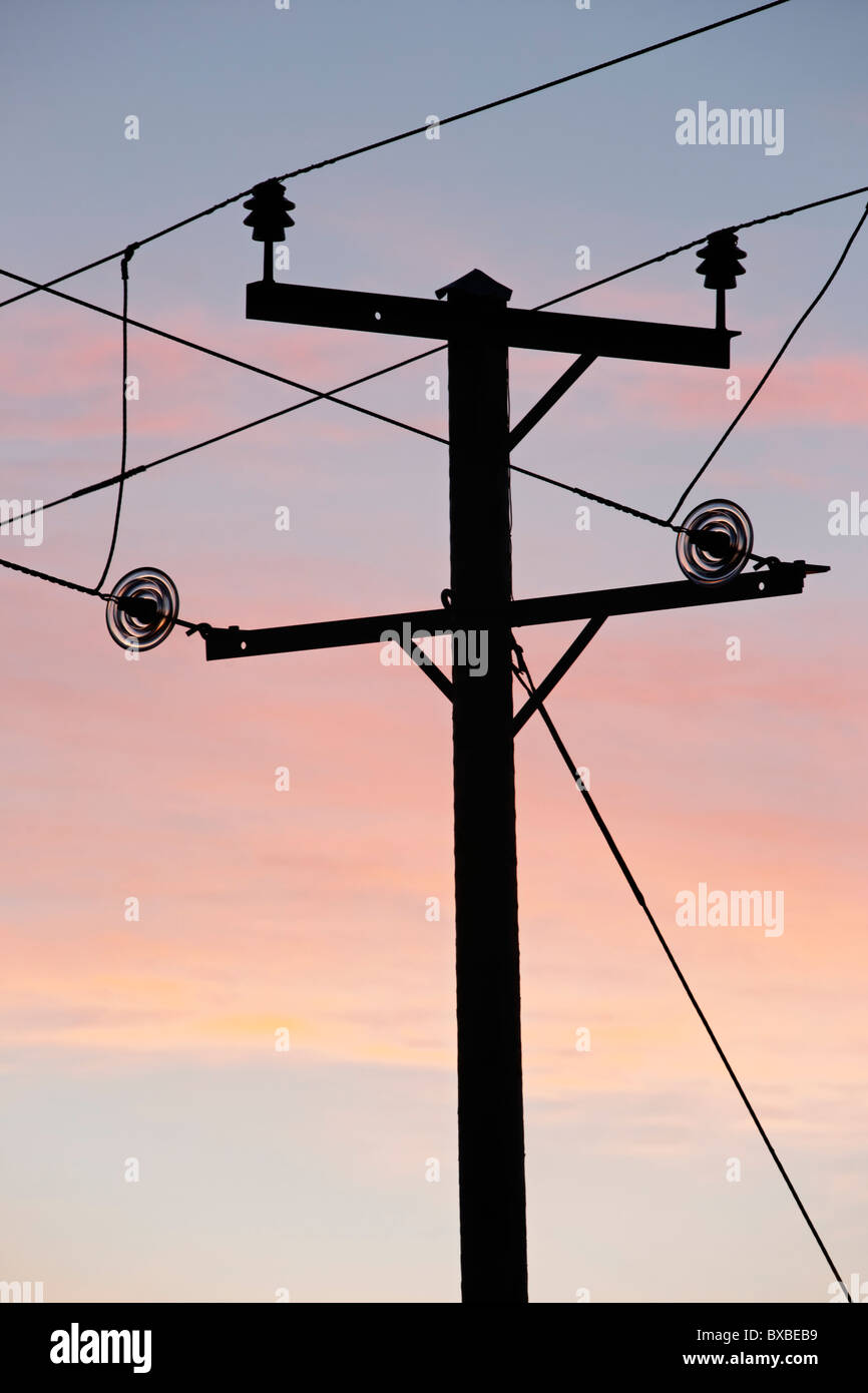 Electricity lines and pole silhouetted against a sunrise sky, Northern Ireland, UK Stock Photo