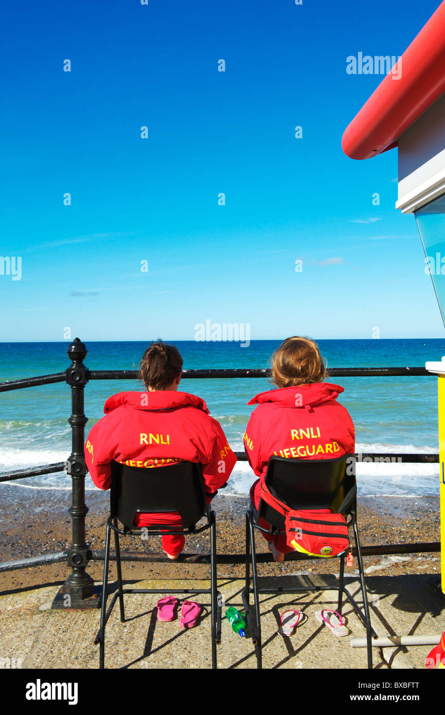 two RNLI female lifeguards sitting looking out to the Norfolk coast on a summers days Stock Photo