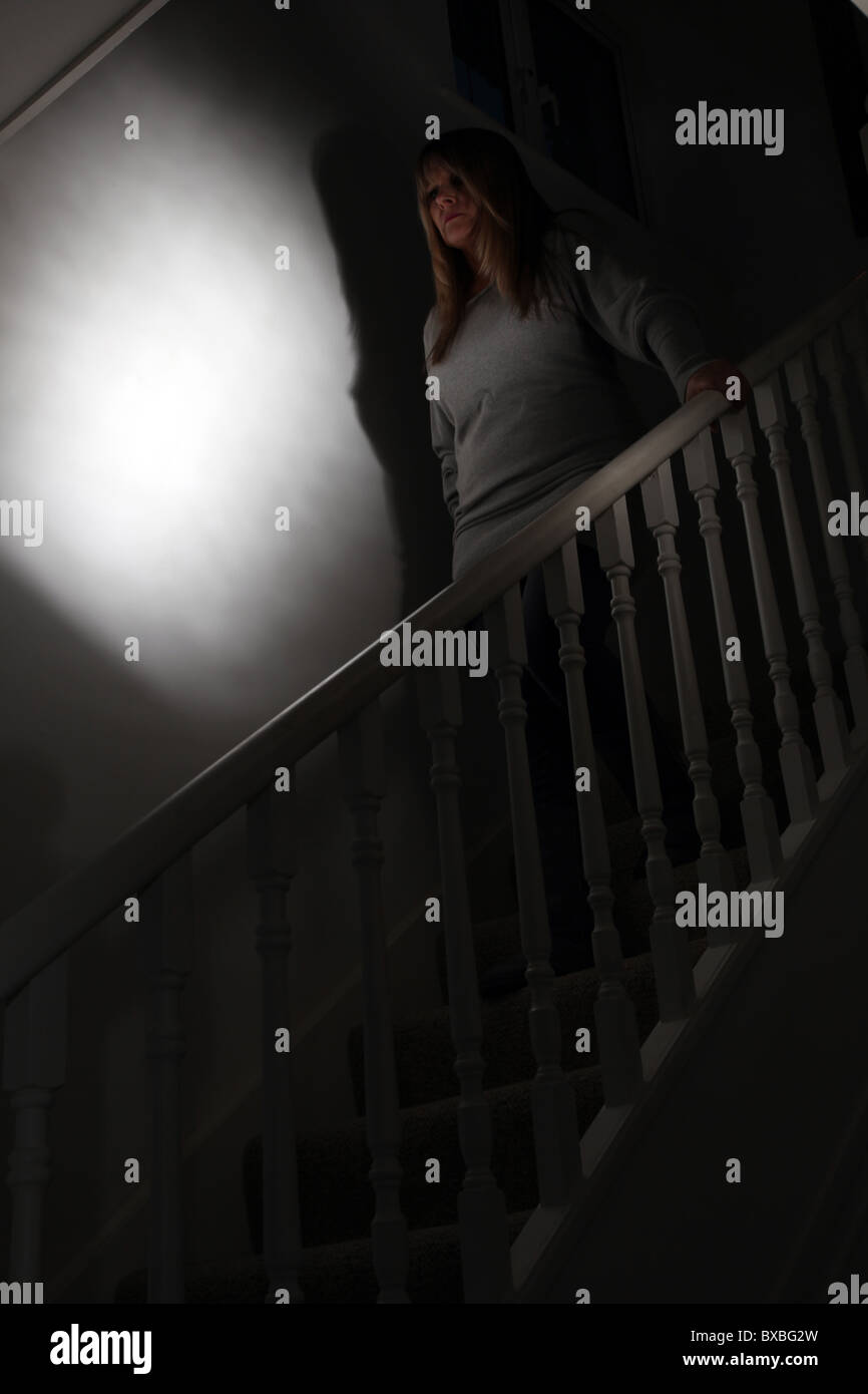 Woman walking downstairs in a dark shadowy room Stock Photo