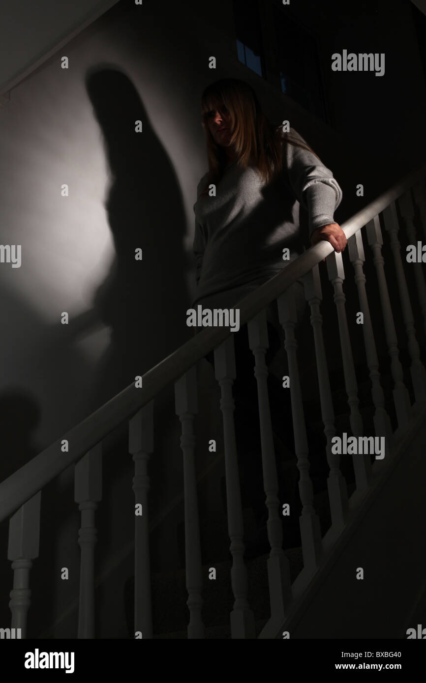Woman walking downstairs in a dark shadowy room Stock Photo
