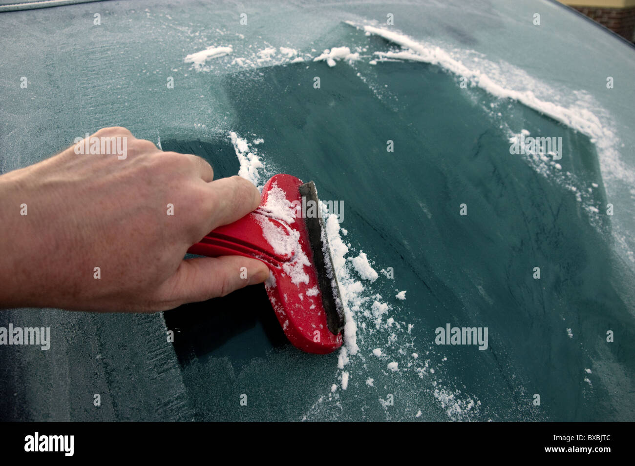 A man's hand holding a scraper, cleaning frost/ice off a car windscreen