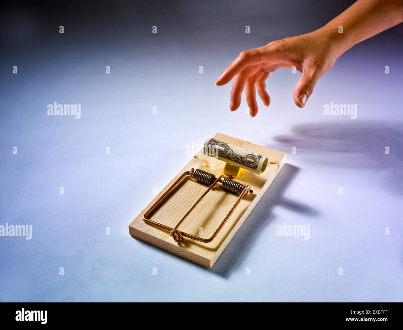 Hand attempting to remove money from large mouse trap Stock Photo
