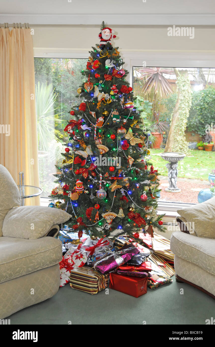 Daytime view of Xmas presents below Christmas tree in home lounge with view to garden beyond Essex England UK Stock Photo