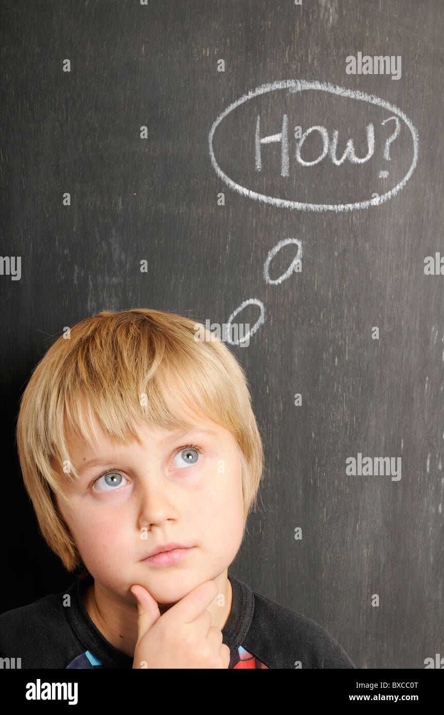 Stock photo of a young boy in front of a blackboard with chalk thought bubbles spelling the word how Stock Photo