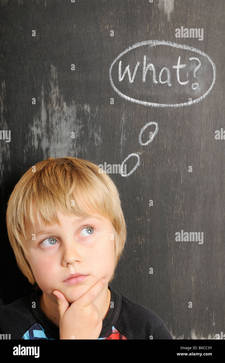 Stock photo of a young boy in front of a blackboard with chalk thought bubbles spelling the word What. Stock Photo