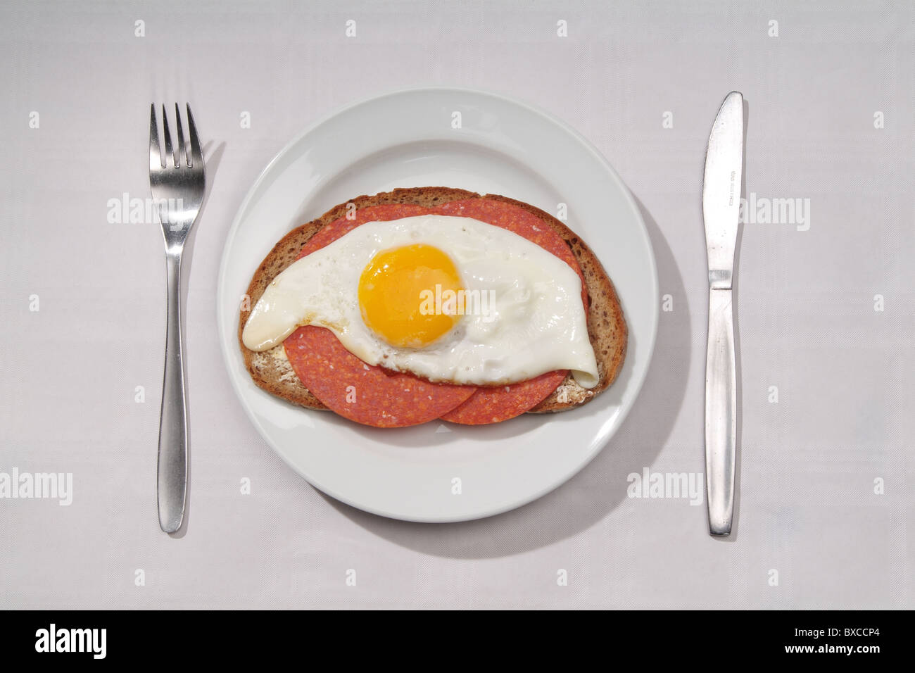 A slice of bread topped with salami and fried egg Stock Photo