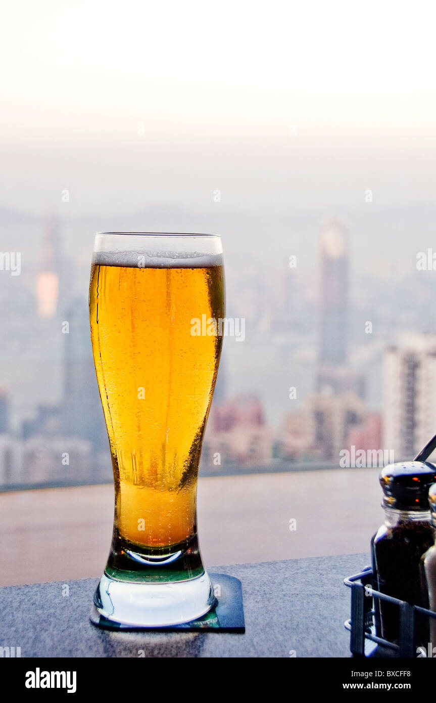 Tall glass of frothy cold beer sitting on bar counter with downtown Hong Kong in background Stock Photo