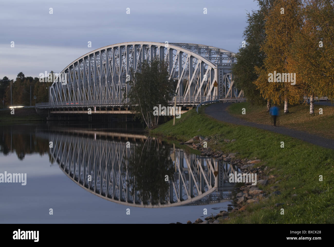 A railroad bridge reflects from the calm waters of river Oulu, Finland. The trees are glowing with autumn tints. Stock Photo