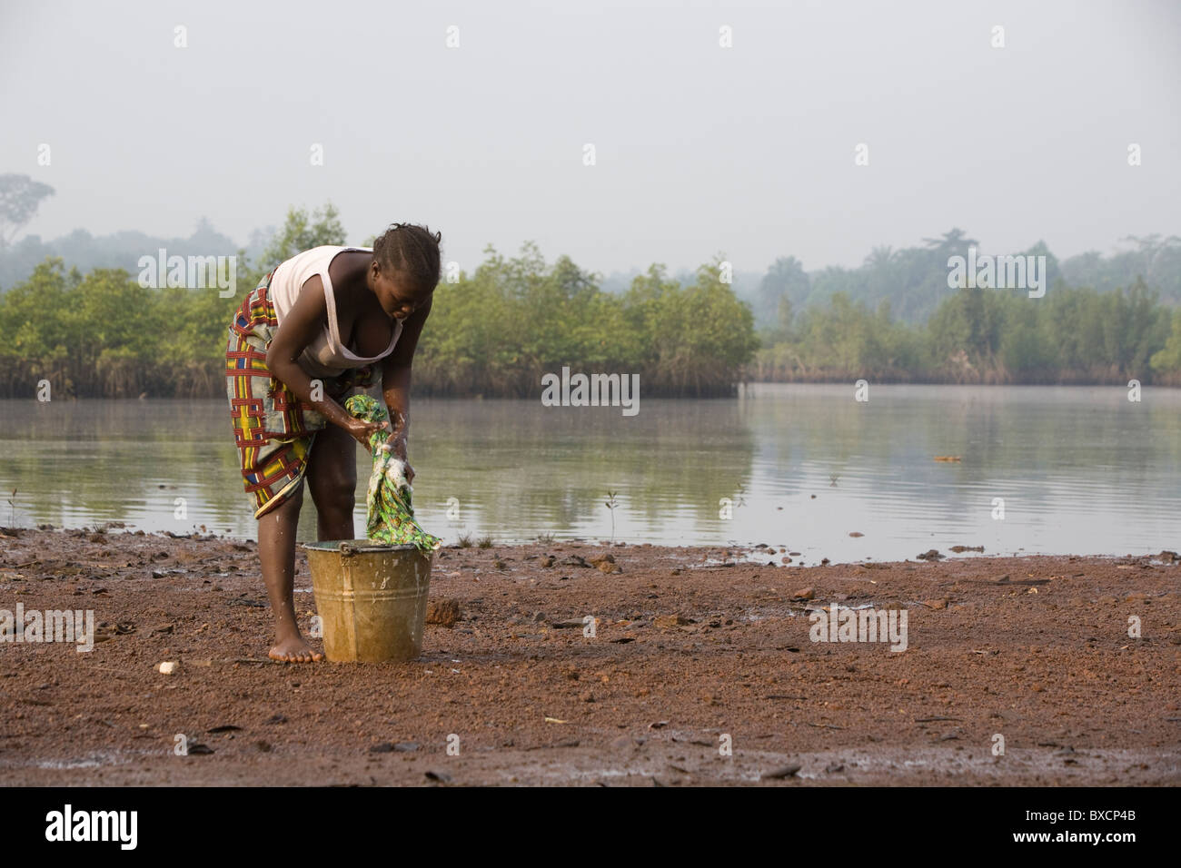 A woman washes clothes in the Sierra Leone River, which runs through the town of Port Loko, Sierra Leone, West Africa. Stock Photo
