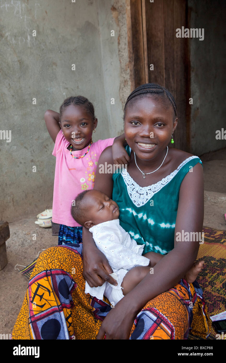 A young mother and her two children sit together on their porch in Port Loko, Sierra Leone, West Africa. Stock Photo