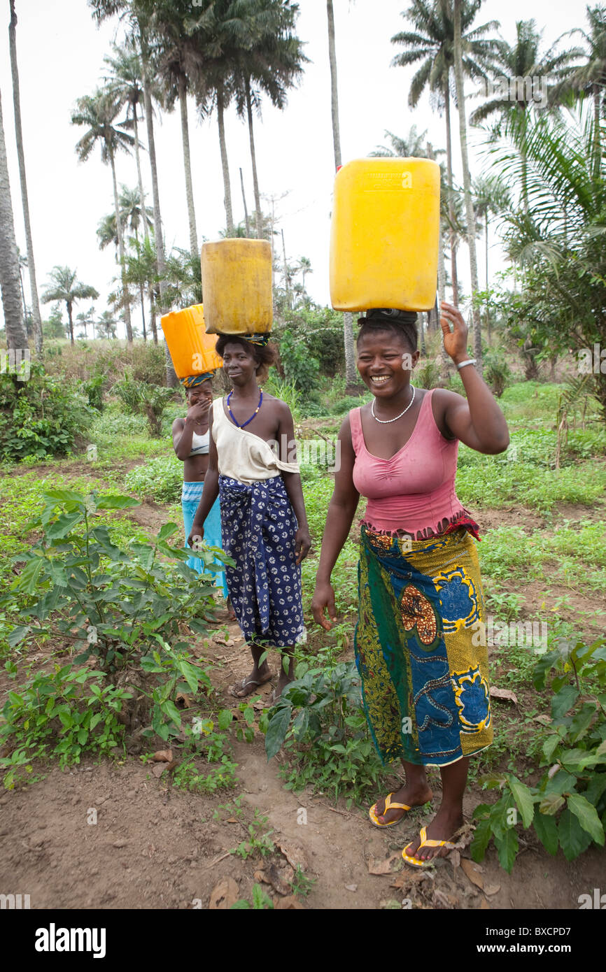 Women carry water back from the well in Masiaka, Sierra Leone, West Africa. Stock Photo