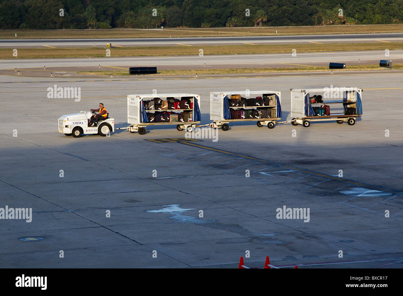 Airport worker drives airport vehicle with luggage to airplane on
