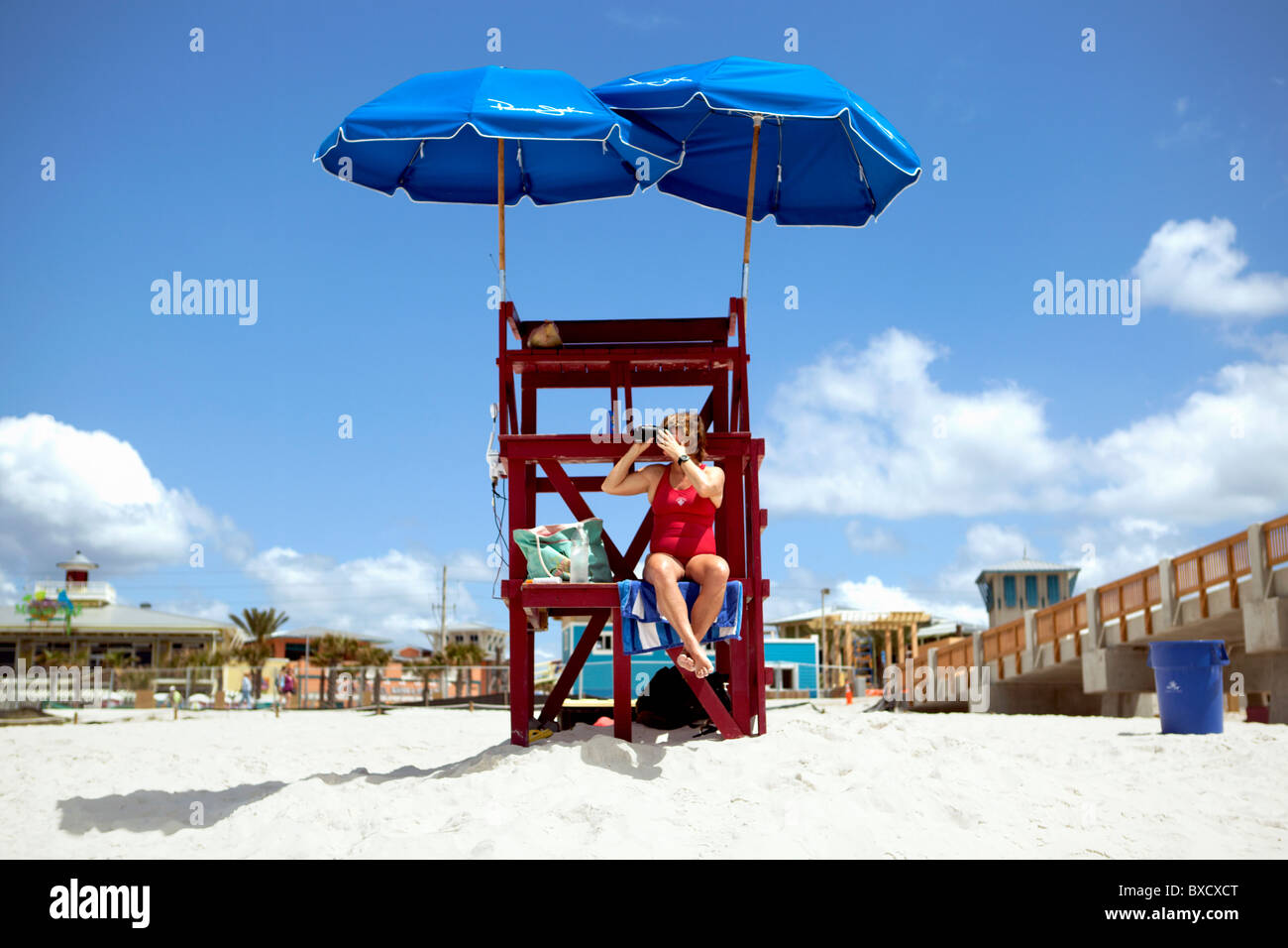 A Lifeguard looking through binoculars and sitting on a red stand.. Stock Photo