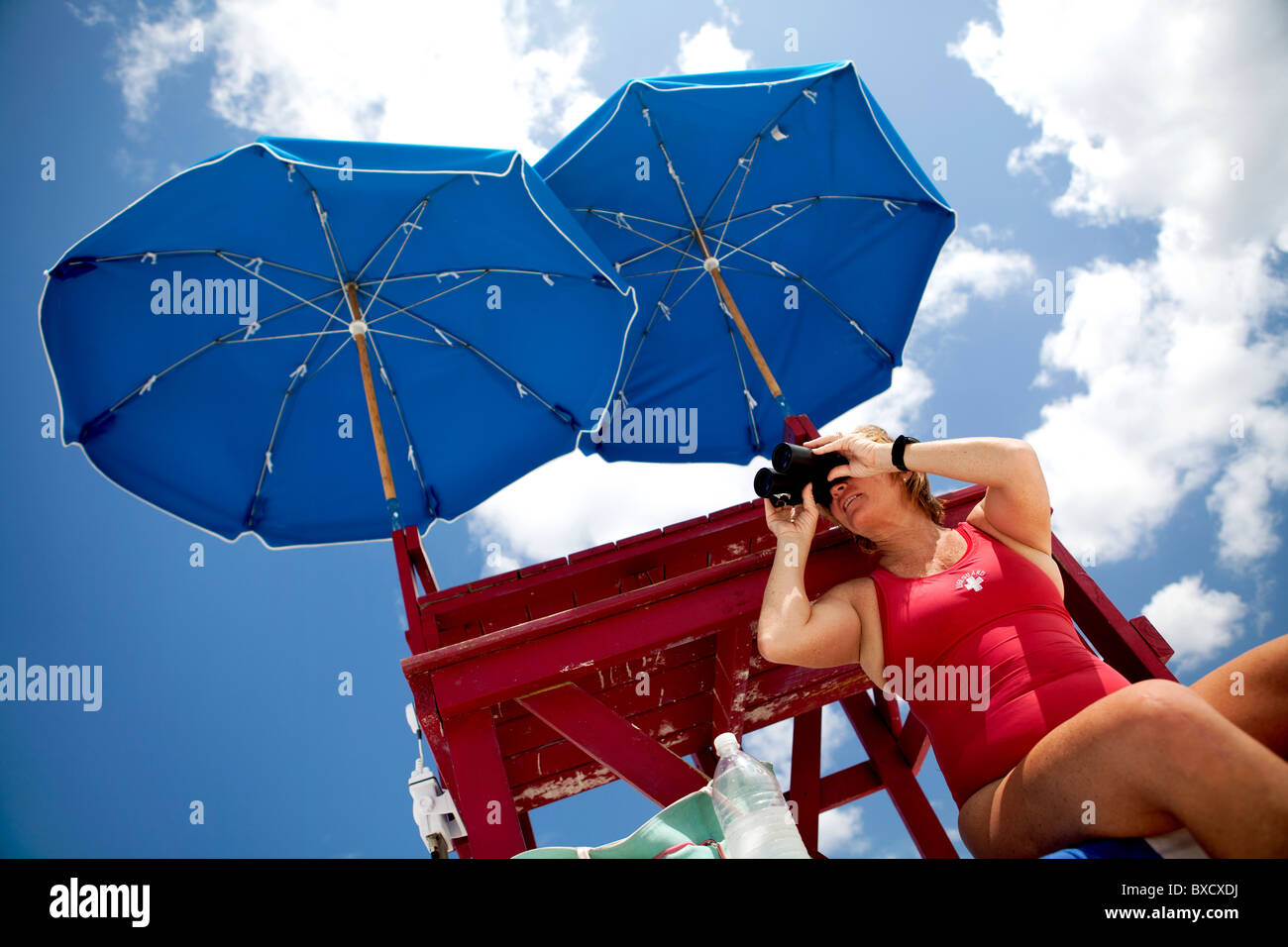 A Lifeguard looking through binoculars under umbrellas. Stock Photo