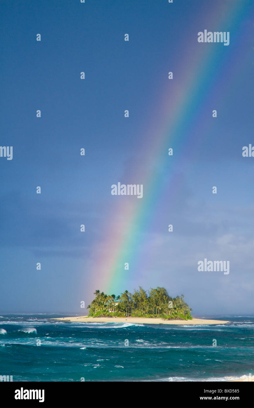 A brilliantly colored rainbow falling over a small desert island. Stock Photo