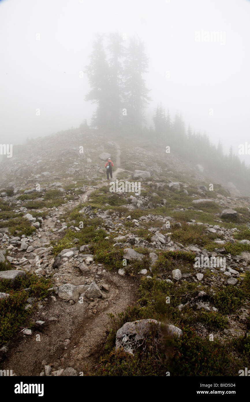 A climber descends a winding trail on a foggy morning on a ridge. Stock Photo