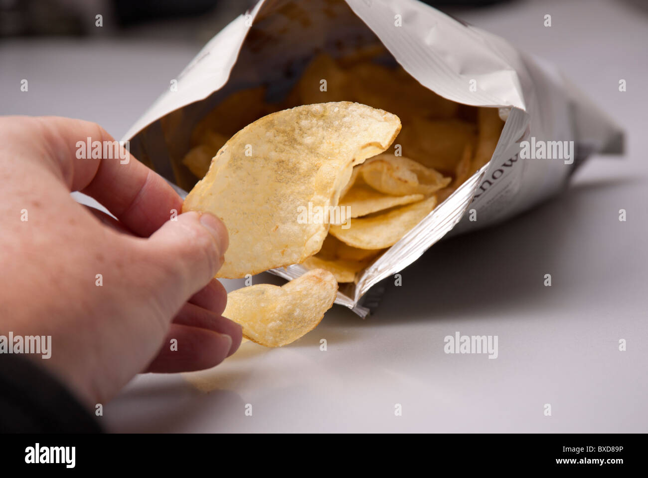 man taking a crisp out of a bag of crisps Stock Photo