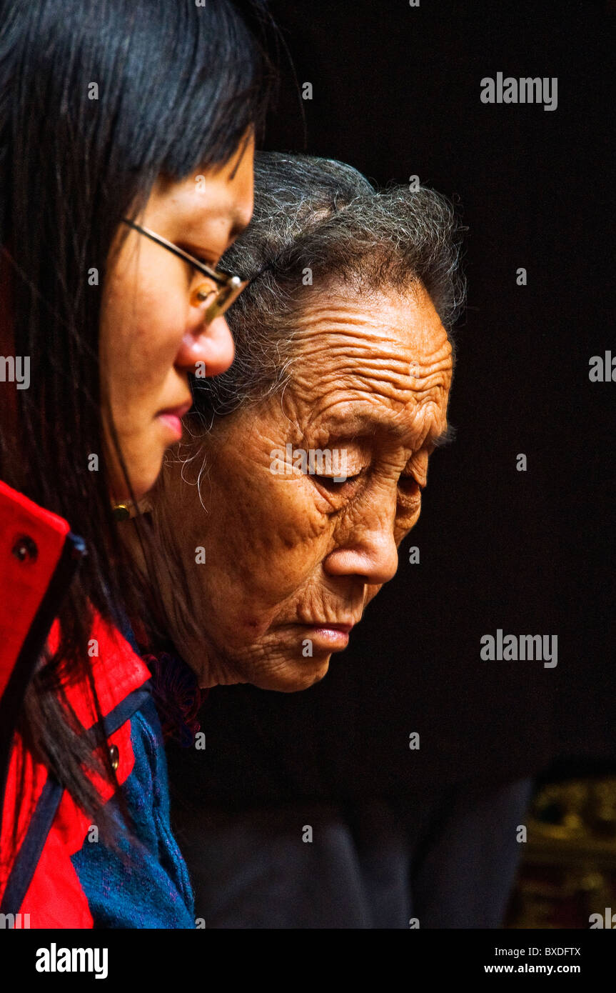 Portrait profiles of young and old Asian women making offering in Buddhist temple Stock Photo